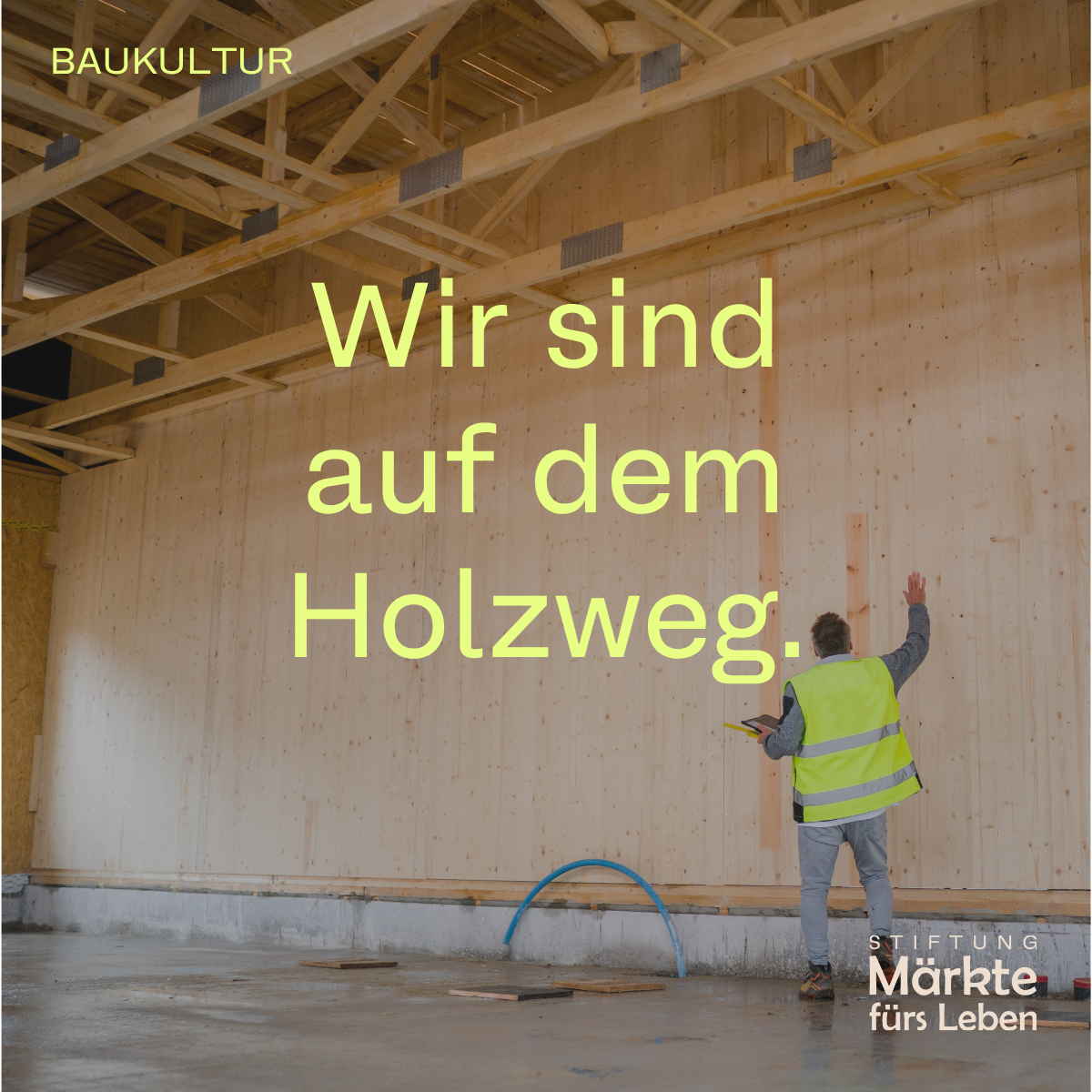 Ein Mann in reflektierender Weste inspiziert eine Holzwand in einem unfertigen Raum. Er hält ein Tablet und berührt die Wand.